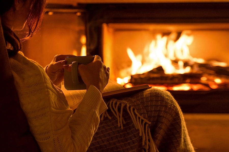 A young woman sitting at home by the fireplace with a mug and a book in Madison County, IL.